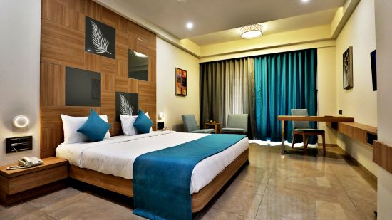 Double bed with blue pillows and bed runner with a wall mounted tv opposite it inside Deluxe Room - VITS Devbhumi, Dwarka