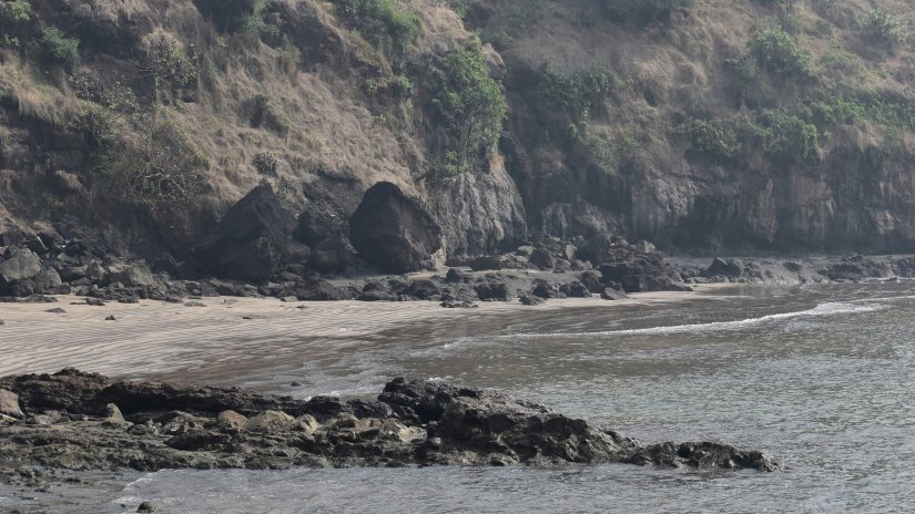 an overview of Alibaug Beach with rocks near the waters and mountains in the background