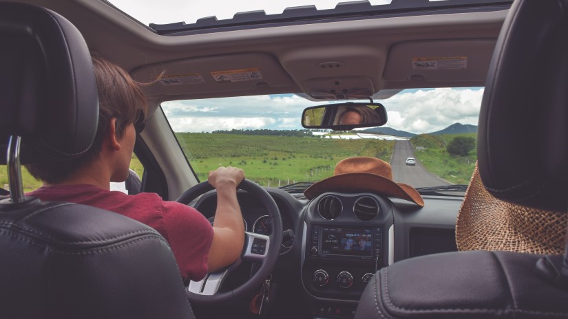 a driver and passenger in a car on a road trip with greenery in view