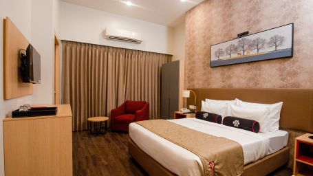 a plush bed with warm toned interiors and room amenities - Mastiff Hotel, Ankleshwar
