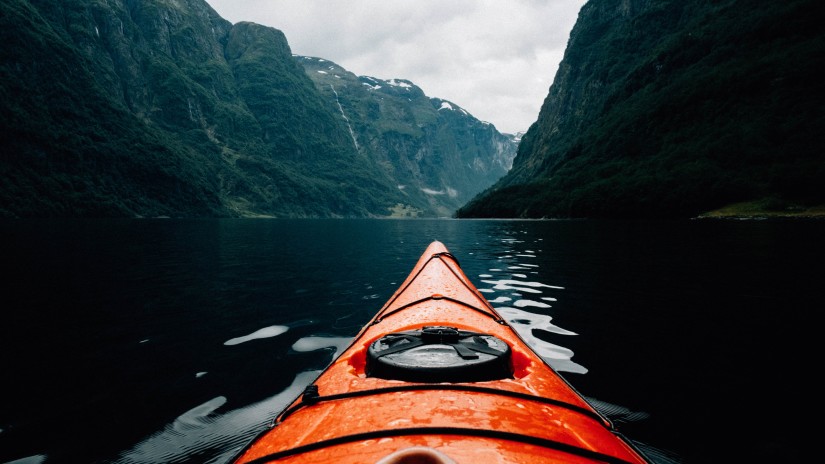 Front view of kayak moving over water with mountains surrounding the area 