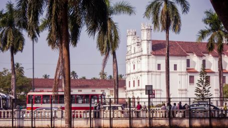 an old church in goa with another building on the side and coconut trees in the foreground