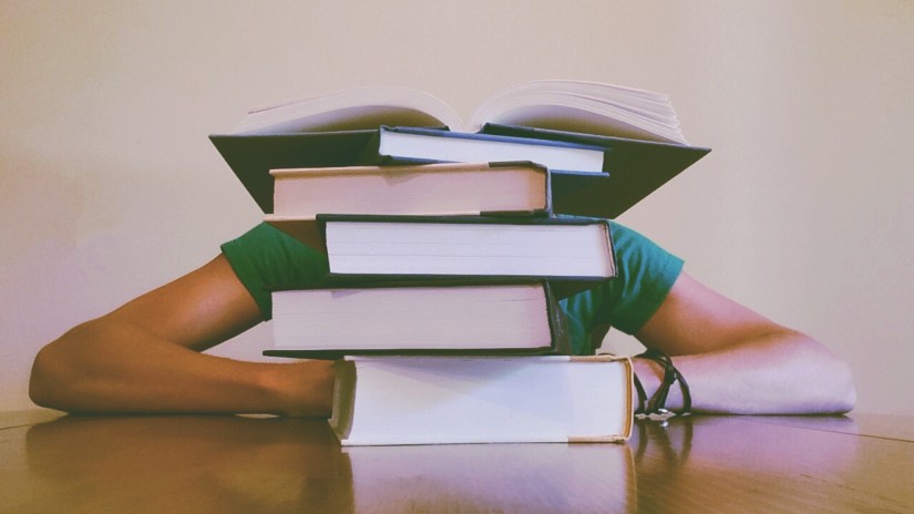 a Person behind a pile of thick books kept in front of him