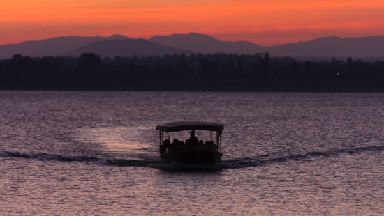 a view of sunset with a boat sailing on the river