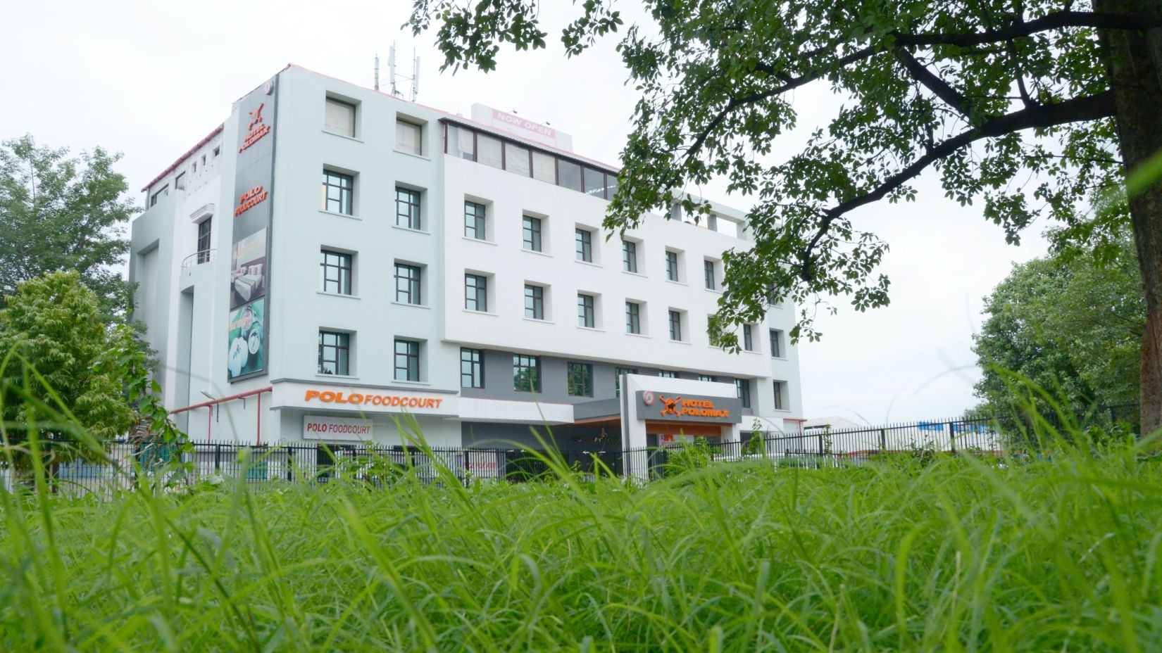 Hotel's facade  viewed from behind vibrant green foliage | Max Hotel Prayagraj.