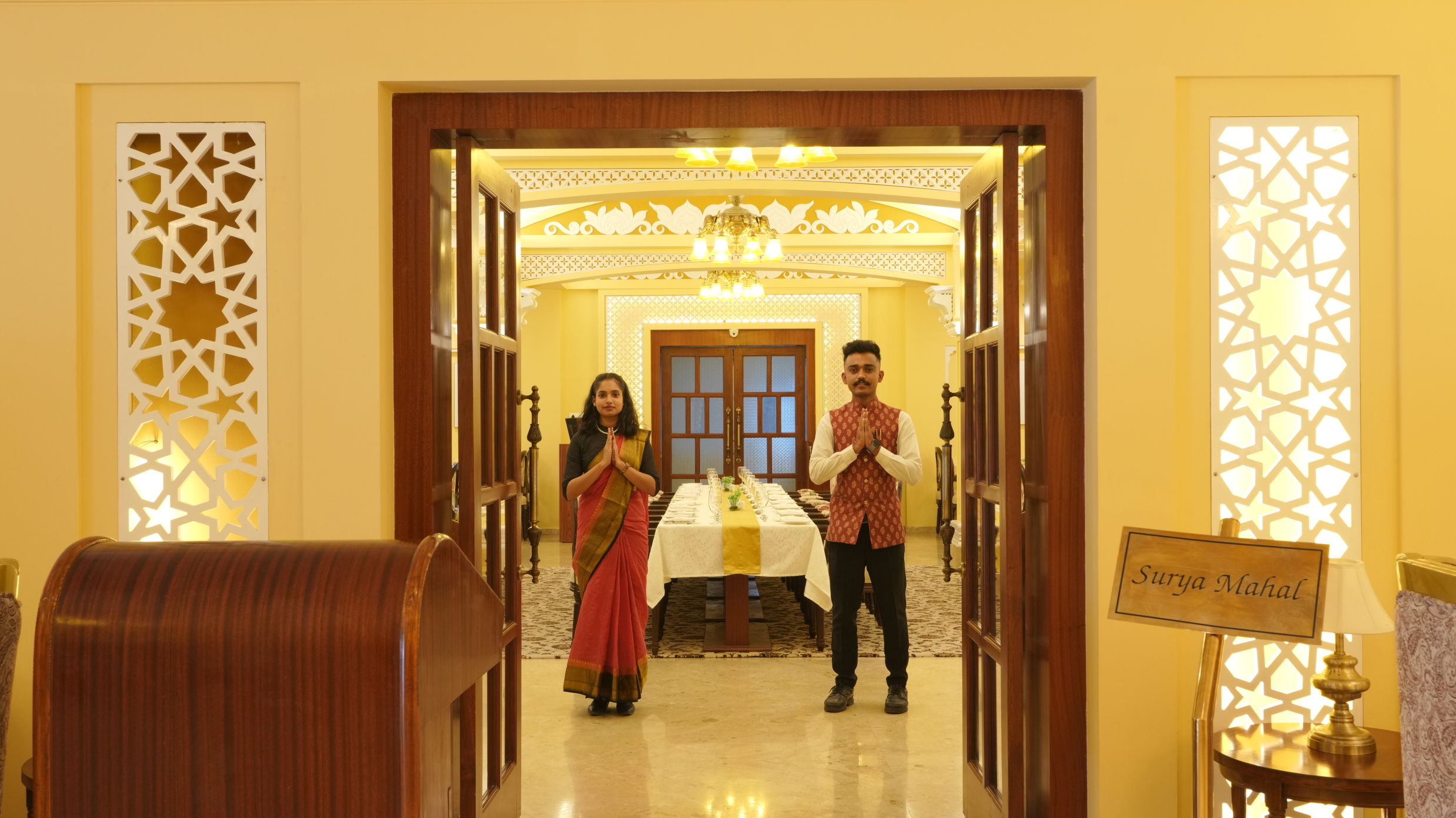 Two receptionists welcoming guests inside the gates of  Suryamahal, the in-house restaurant at The Garden Ananta Elite, Rajkot