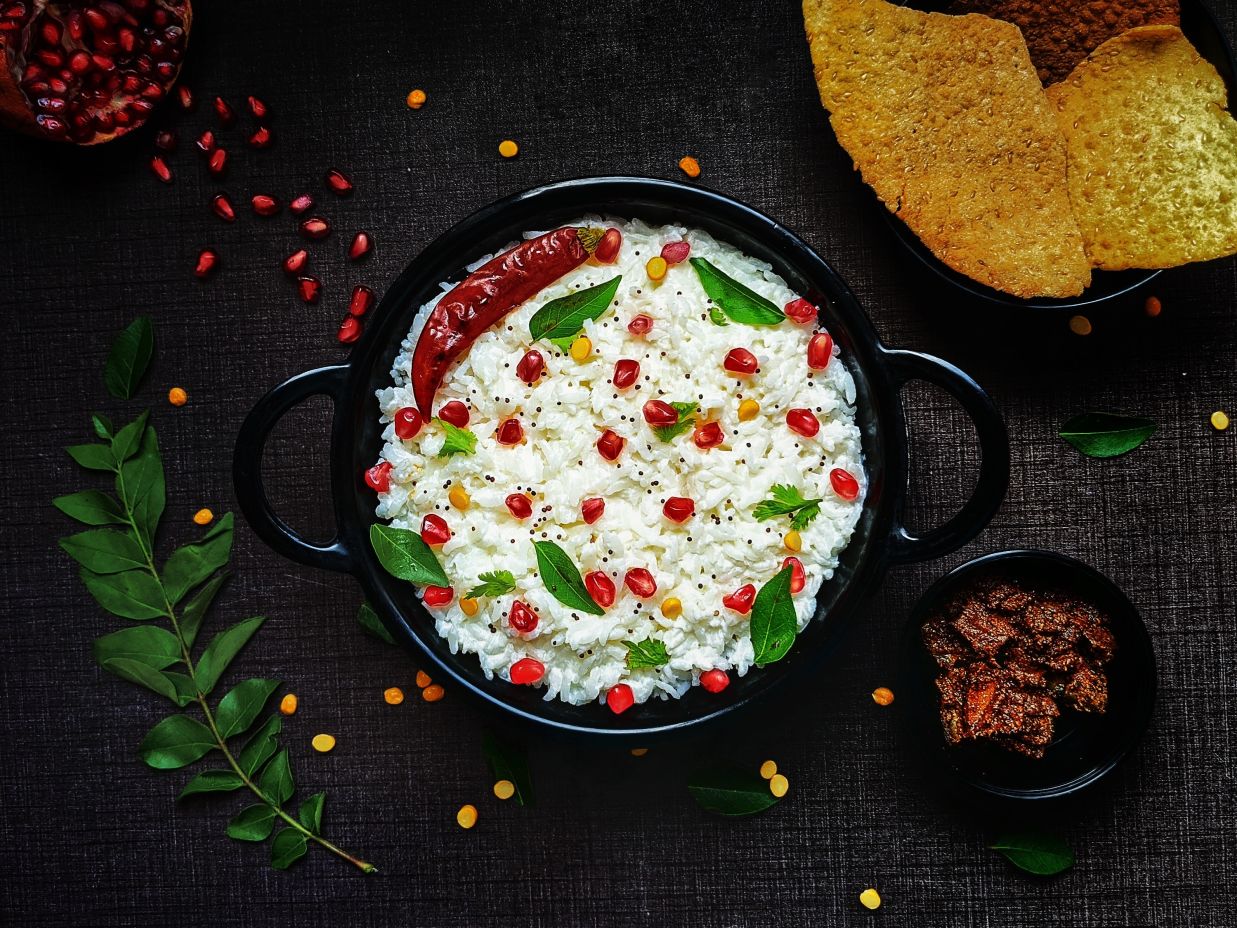 Image of a rice-based dish with curry leaves and pomegranate as props