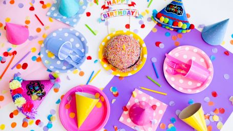 a table with many birthday party items like hats, plates, confetti and more with a small happy birthday banner as well