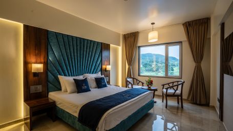 View of Suite with king sized bed and bedside tables seating area with windows and curtains - Mastiff Grand - The Sia Palace Suites Banquets Khopoli