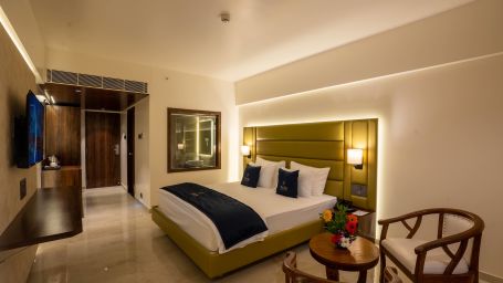 Side view of Deluxe King with plush bed and bedside tables seating area TV set coffee and tea maker and partial view of the washroom - Mastiff Grand - The Sia Palace Suites Banquets Khopoli
