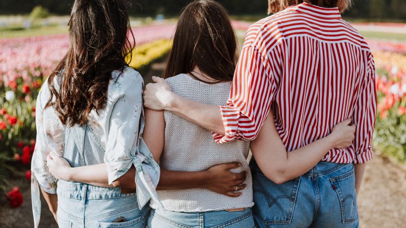 three girls hugging each other from the side in front of a flower field