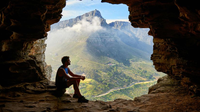 image of a man sitting at the entrance of a cave in the mountains in Cherrapunji sightseeing