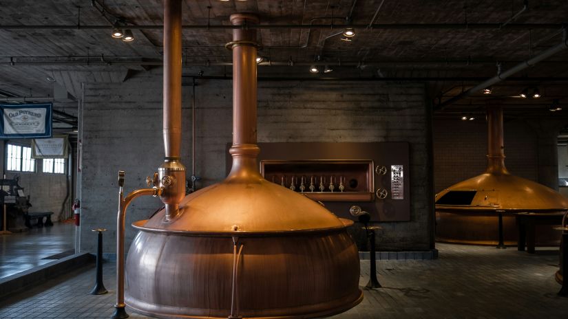 Image of a large copper brewing kettle in a bright industrial brewery.