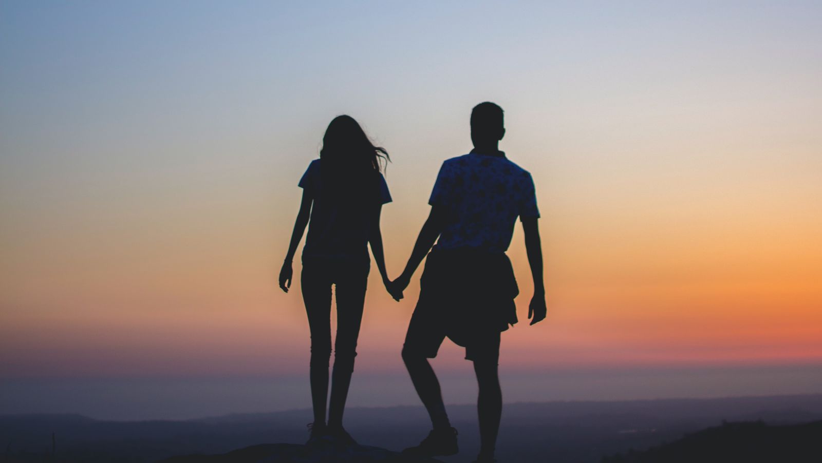 Silhouette of couple holding hands as they watch sunset