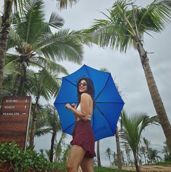 woman with black sunglasses and maroon skirt holding a blue umbrella