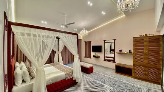 a king size bed along with a chandelier hanging from top, cupboards and a mirror offered at Moghul room - Zara's Resort