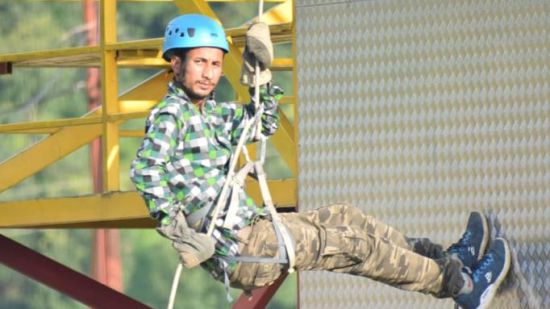 An adventurer in safety gear rappels down a yellow structure with a determined expression, showcasing the thrill of the activity.