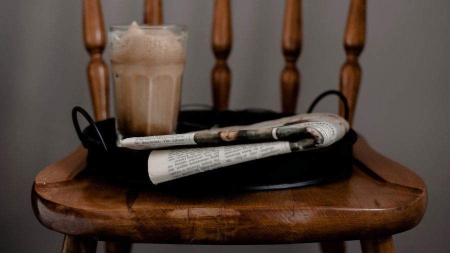 Foamy coffee and newspaper served on tray placed on chair