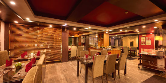 Renest Hotel Manali - Interior view of the restaurant featuring numerous seating options in brown and red decor 