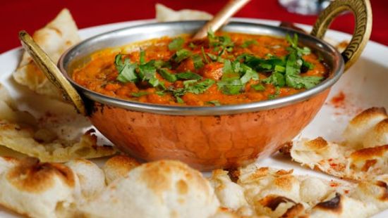 Image of a bowl of curry with naan on the side of the plate