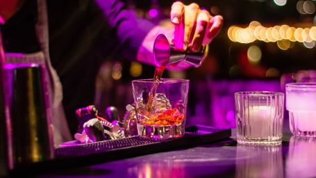 A bartender pouring a drink on a glass that is placed on a bar counter