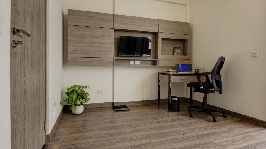 A study table and a tv wall mounted inside a wooden cabinet inside Premium Suite - Rhythm Gurugram