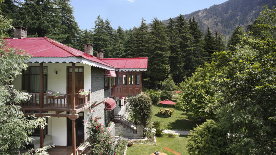 Side view of the facade of Bedzzz Xclusiv Baikunth, Manali surrounded by trees and mountain in the background