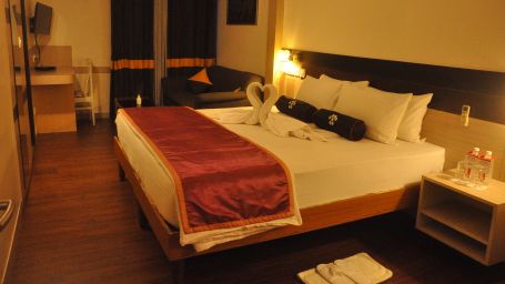 Side angle view of deluxe room with bed side table, TV set and partial view of wardrobe - Mastiff Infantry, Bangalore