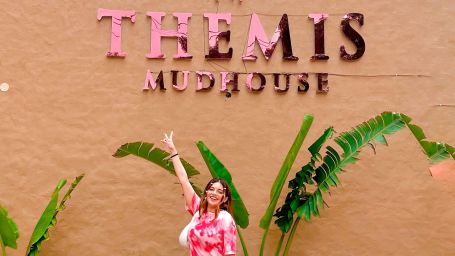 a woman with her luggage standing in front of Themis Mudhouse - A Nature's Retreat Resort & Wellness