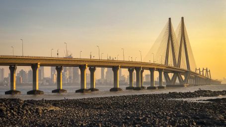  The sun casts a golden glow on a modern cable-stayed bridge towering over a pebbled shore.-Fort JadhavGADH 