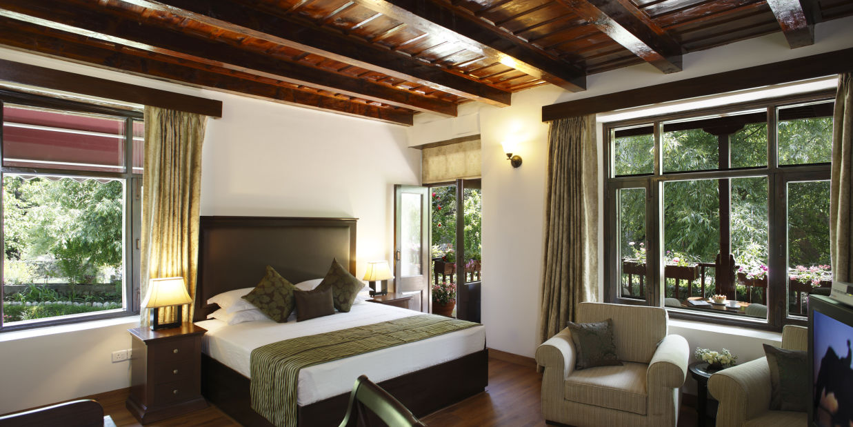 Room wiht bed, sitting area, wooden  ceiling and window overlooking the lush surroundings  at Bedzzz Xclusiv Baikunth, Manali