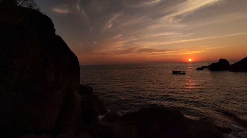 Sun setting in the background with rocks and water in the foreground at Cola Beach in Goa