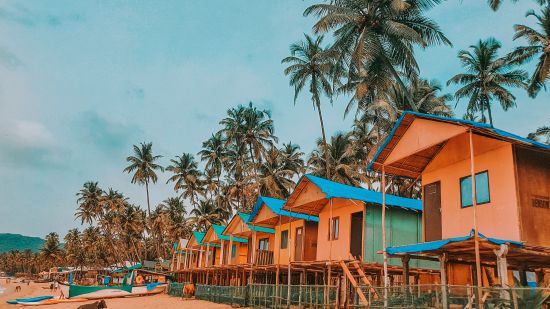 a row of shacks on a beach with coconut trees in the background - birthday celebration in Goa