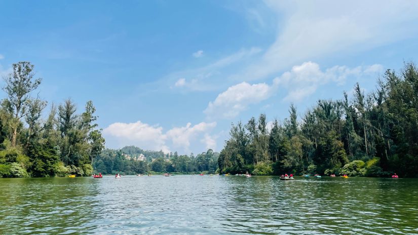 a view of Ooty lake with trees in the background and blue skies 