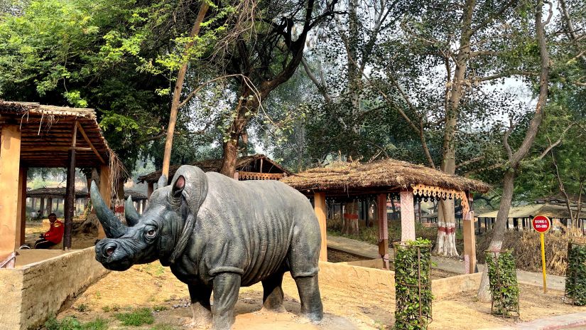 A metal statue of a rhino with greenery around it and trees in the backfround