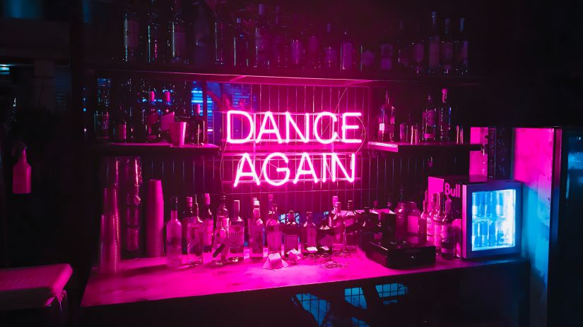 a neon sign with Dance Again mentioned on it and drinks surrounding it