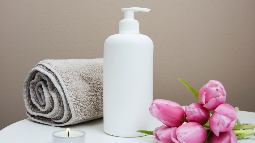 A white lotion bottle, flowers and a rolled up towel