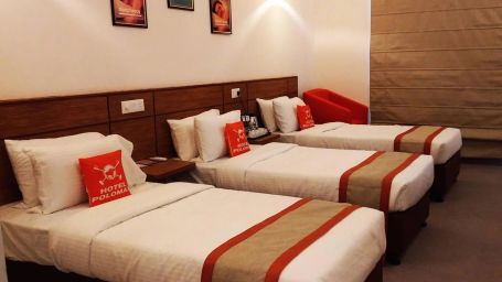 A room in the hotel with three single beds with orange accents, a comfortable seating area, and modern amenities, offering a homely atmosphere.