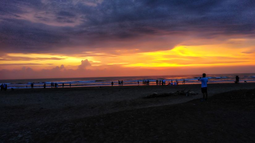 many people on Morjim beach walking and playing after the sunset with different hues in the sky