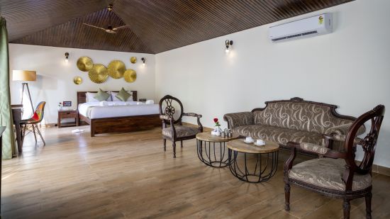 A spacious bed positioned beneath a decorative wallpaper, accompanied by comfortable sofas for relaxation in the room - Stone Wood Nature Resort, Gokarna