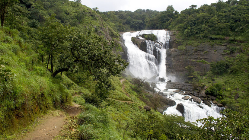 Large waterfall in a green forest with a footpath on the left