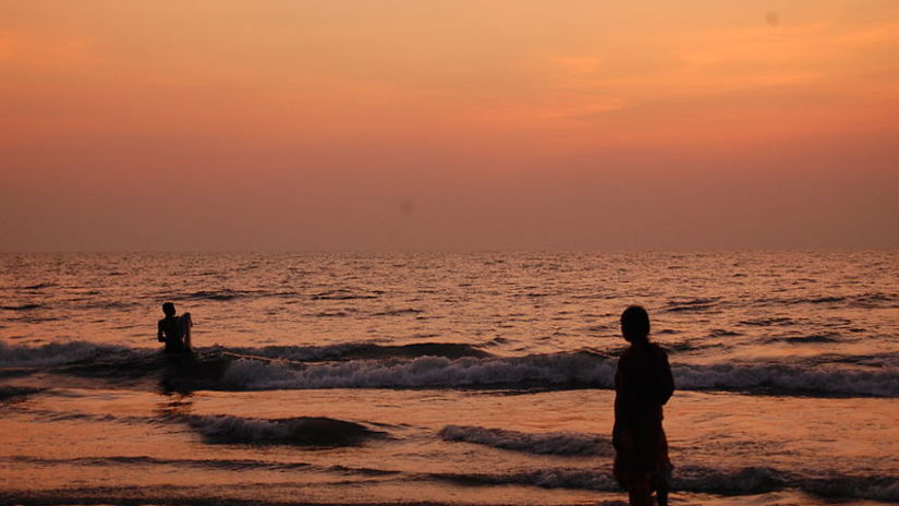 an image of a beach where two people are enjoying the waves during the sunset