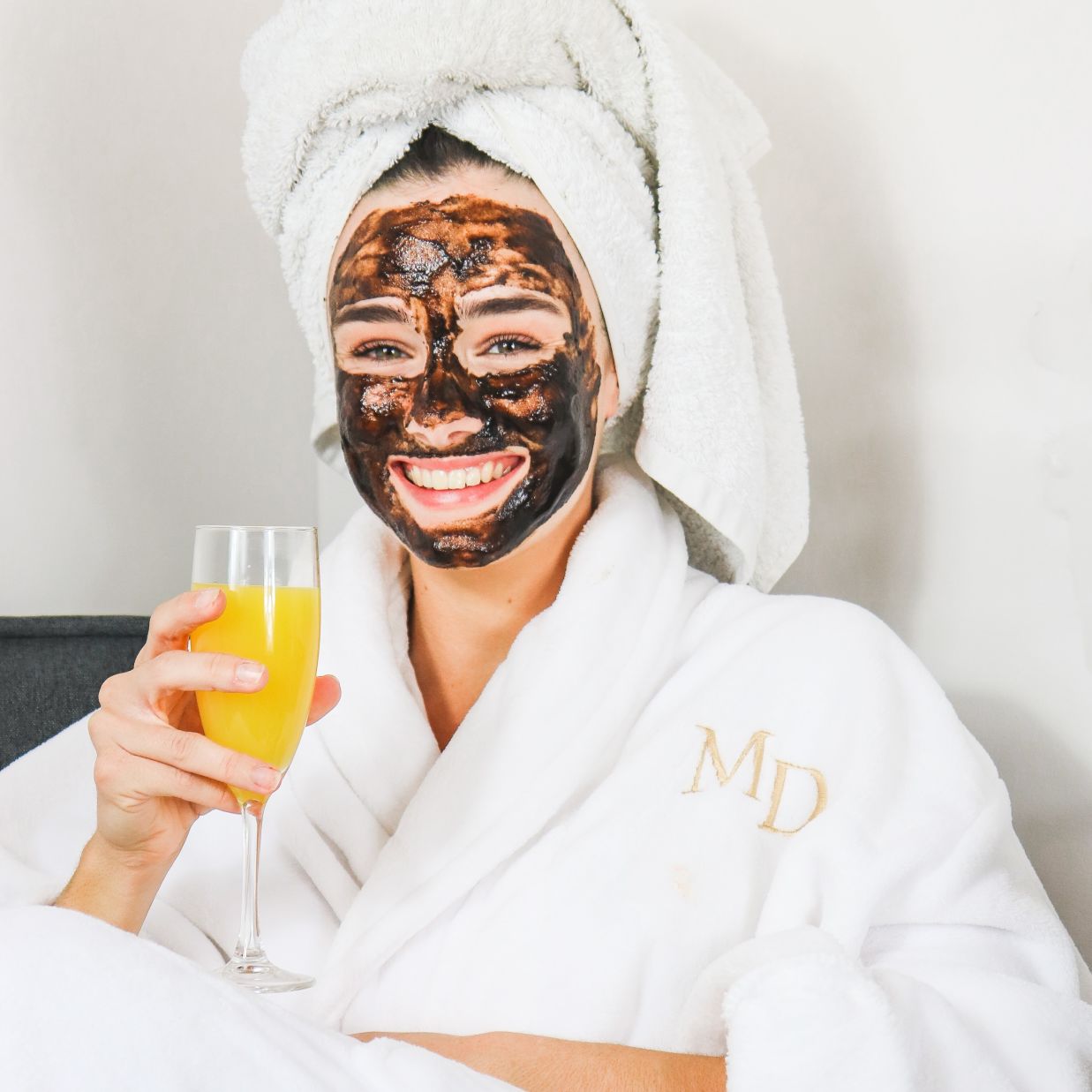 a woman with a face mask in bathrobe holding a glass of juice 