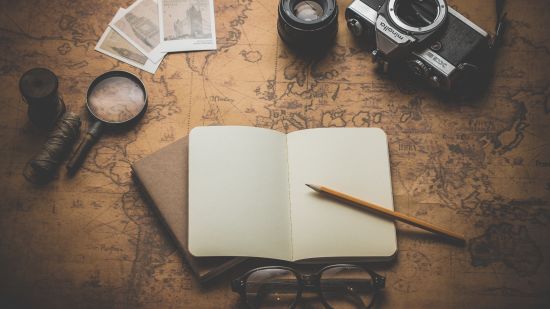 an open notebook placed on top of a map along with pencil, camera and glasses