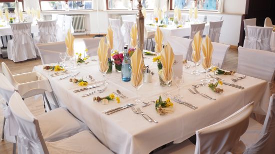 white table with decoration on it surrounded by white chairs in a banquet hall