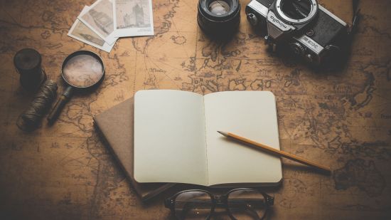 a book, magnifying glass, camera, glass, pencil and polaroid pictures on a table 