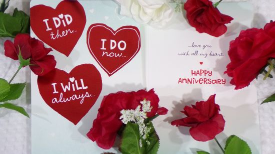 Words written inside red heart shaped decor on a greeting card with a rose on the side