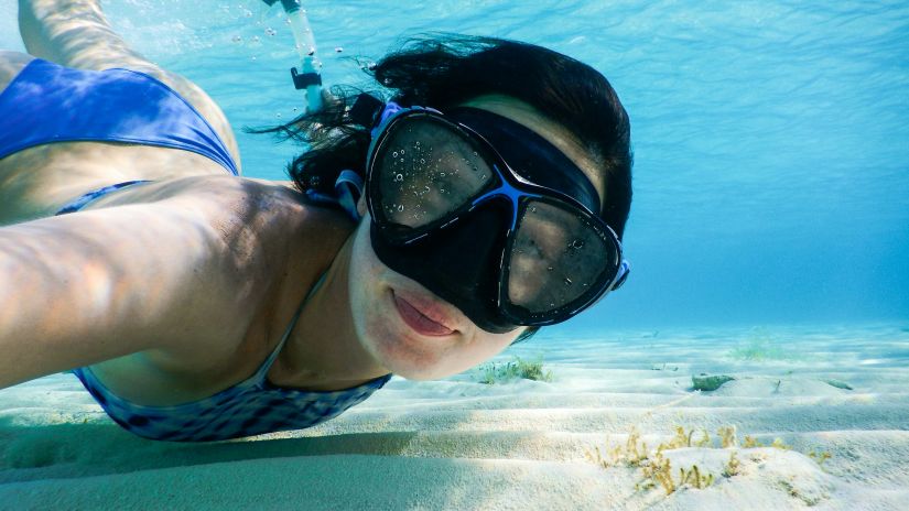 A woman underwater with a snorkelling gear on and looking at the camera while posing for a picture