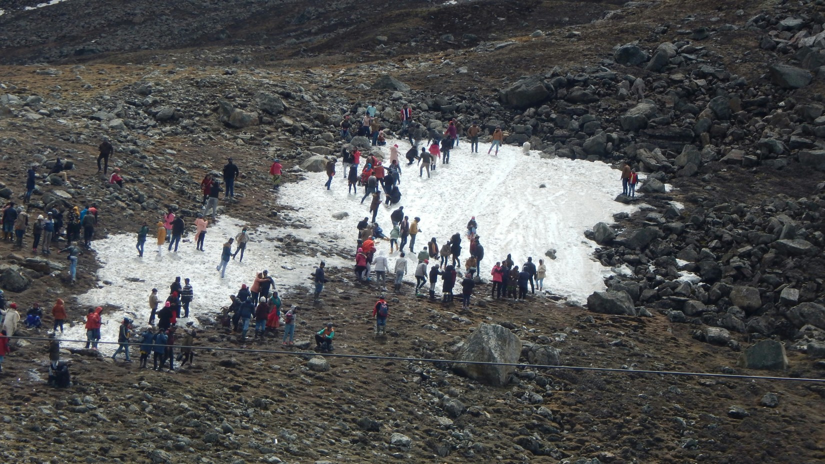 A group of people enjoying a snow patch on a rocky mountain slope