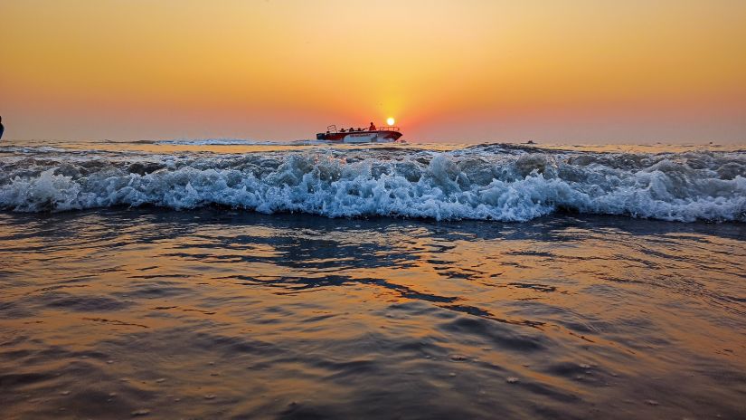 a beach in Mumbai with a ship sailing in between